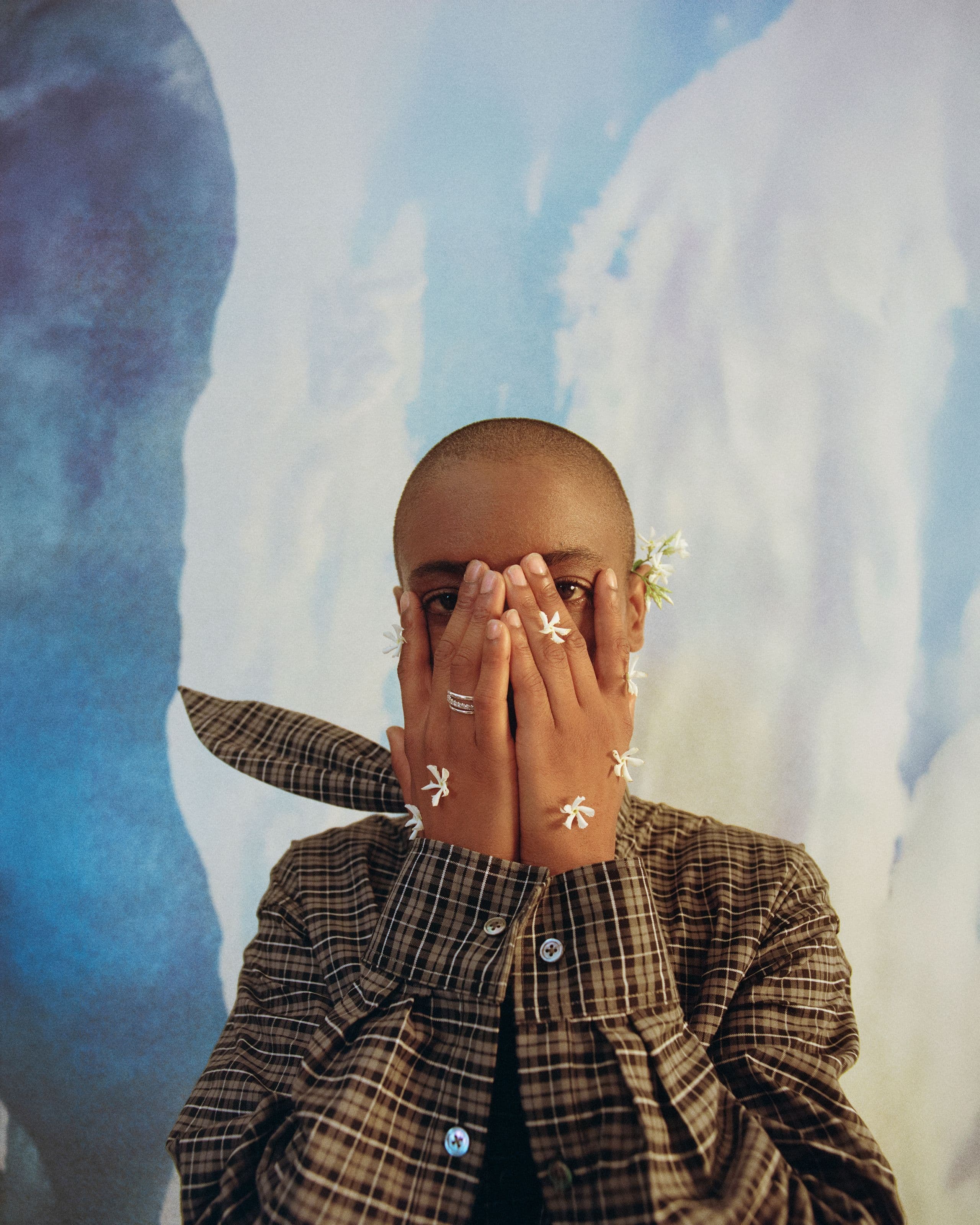 Syd with her hands over her face, flowers on her fingers
